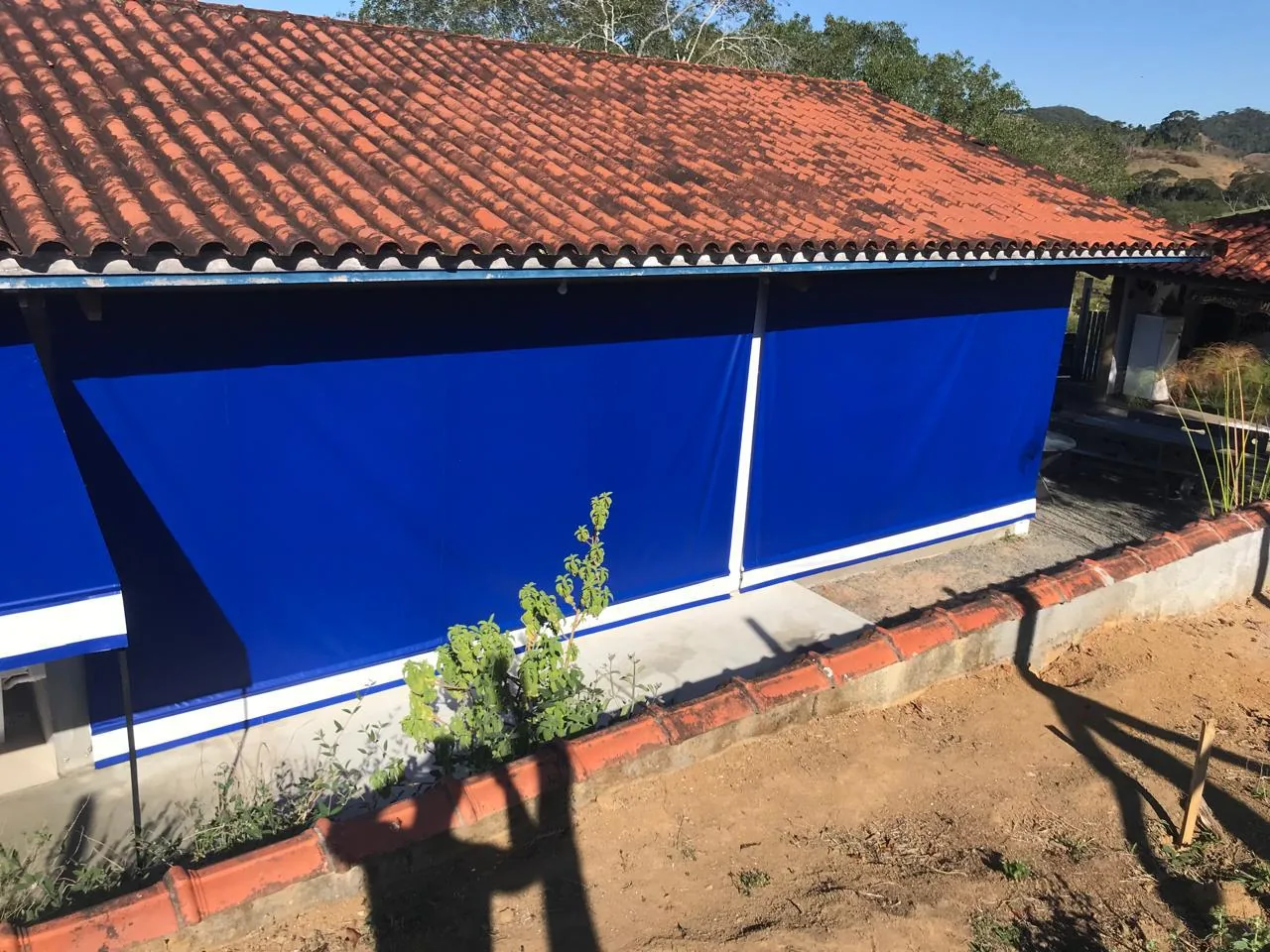 Toldo retrátil com braços em lona azul aberto na lateral de uma casa em Rio Pomba