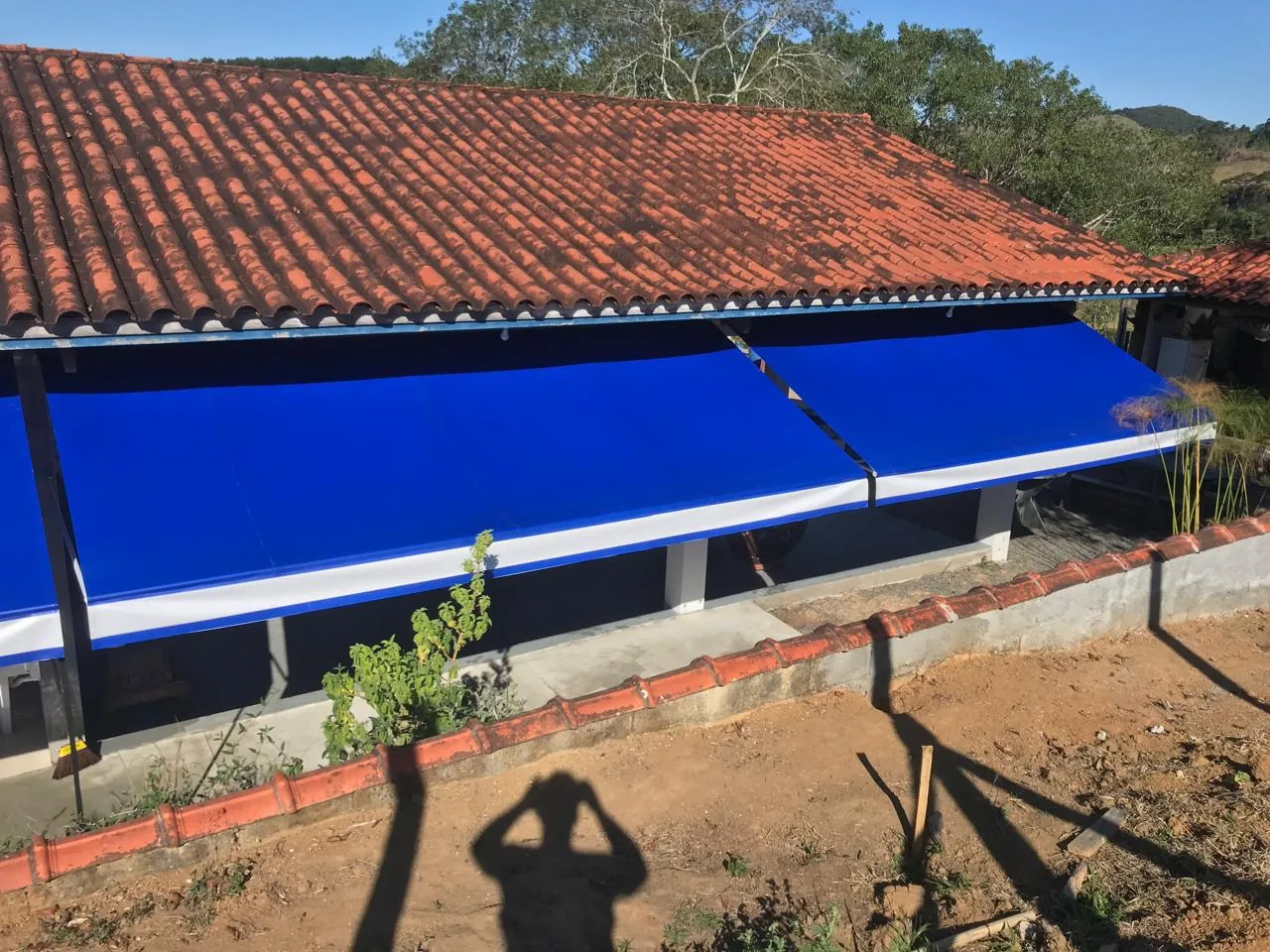 Toldo retrátil com braços azul instalado em toda a extensão da parede