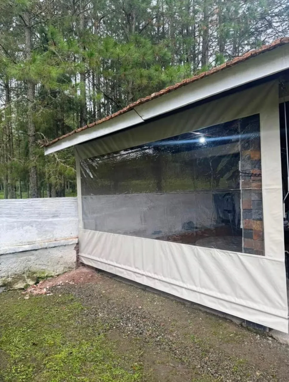 Toldo cortina em lona clara com visor transparente instalado na lateral de uma casa