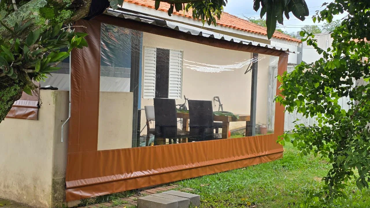 Toldo cortina laranja com visor cristal fechando área externa com mesa e cadeiras